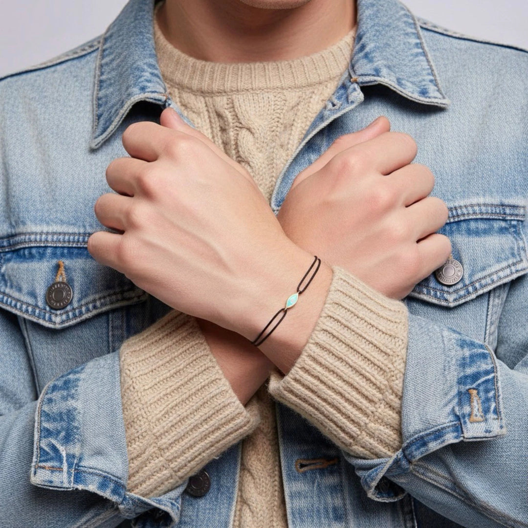 Person wearing a denim jacket and beige sweater with a bracelet on a plain background