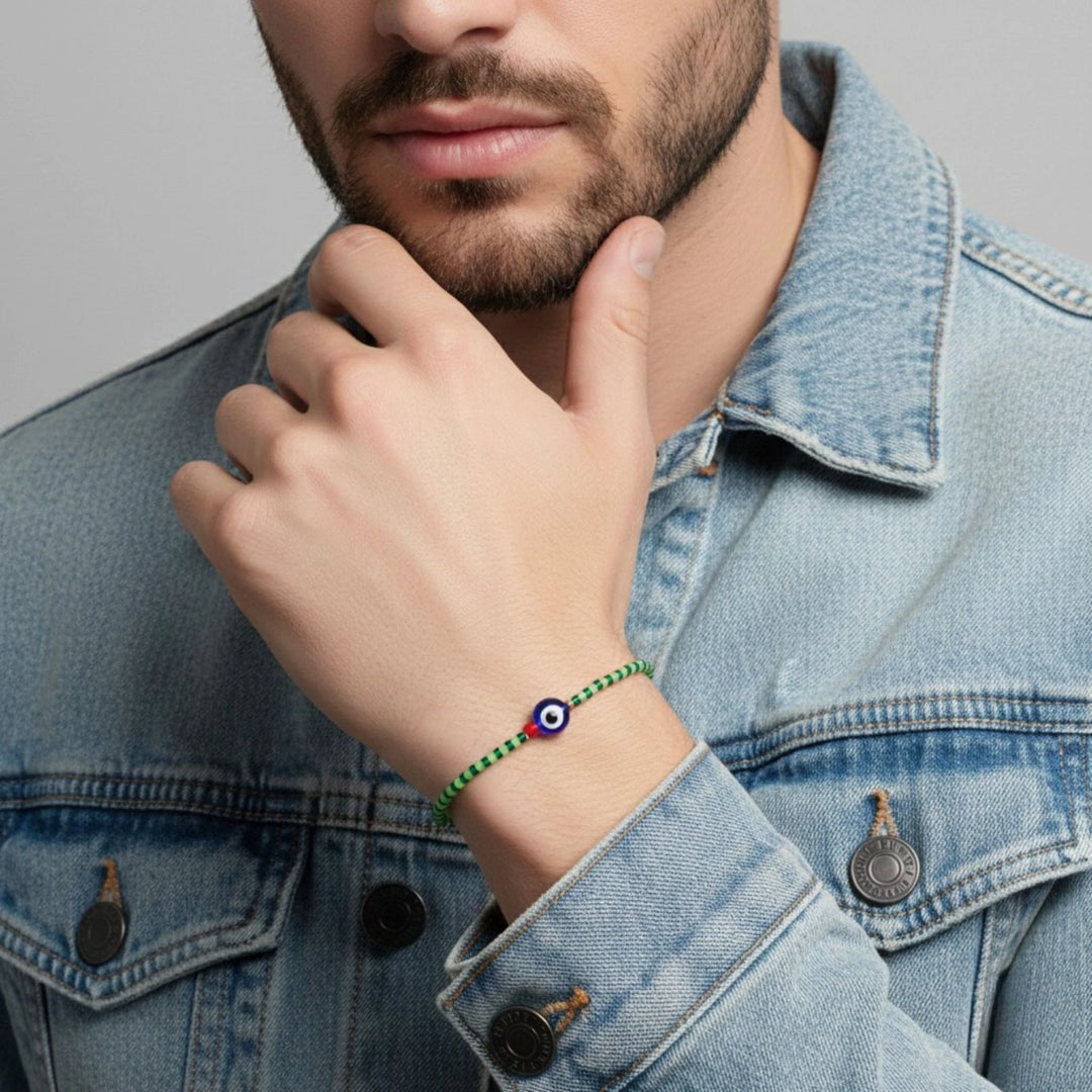 Man wearing a green bracelet with a blue and red evil eye charm on a gray background