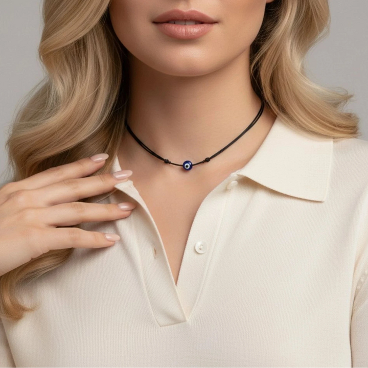 Woman wearing a necklace with a blue evil eye  pendant against a neutral background