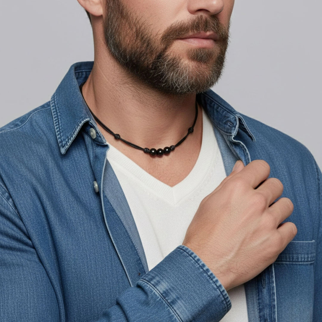 Man wearing a blue denim jacket and white shirt with a black beaded necklace.