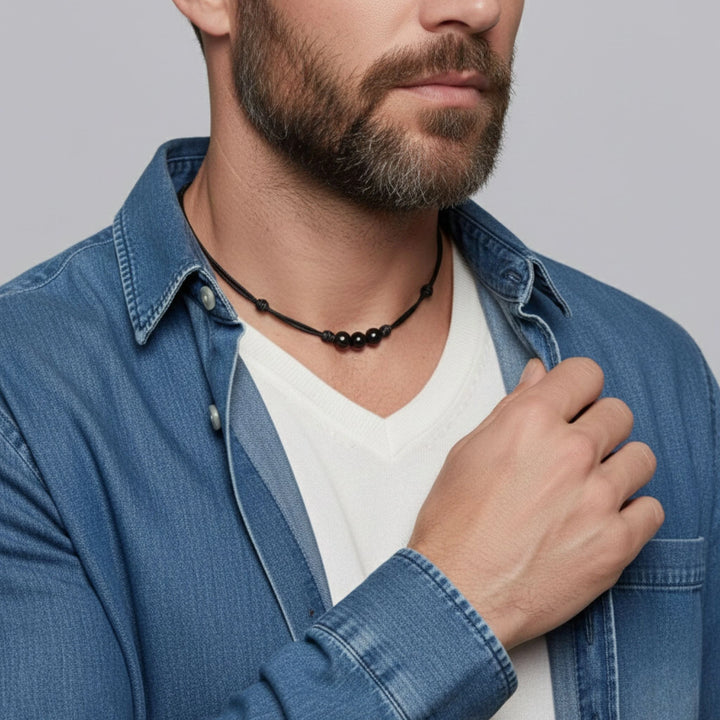 Man wearing a blue denim jacket and white shirt with a black beaded necklace.
