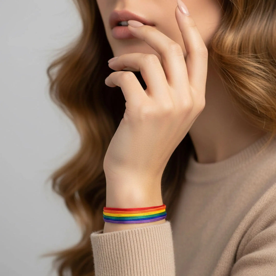 Person wearing a rainbow bracelet on a neutral background