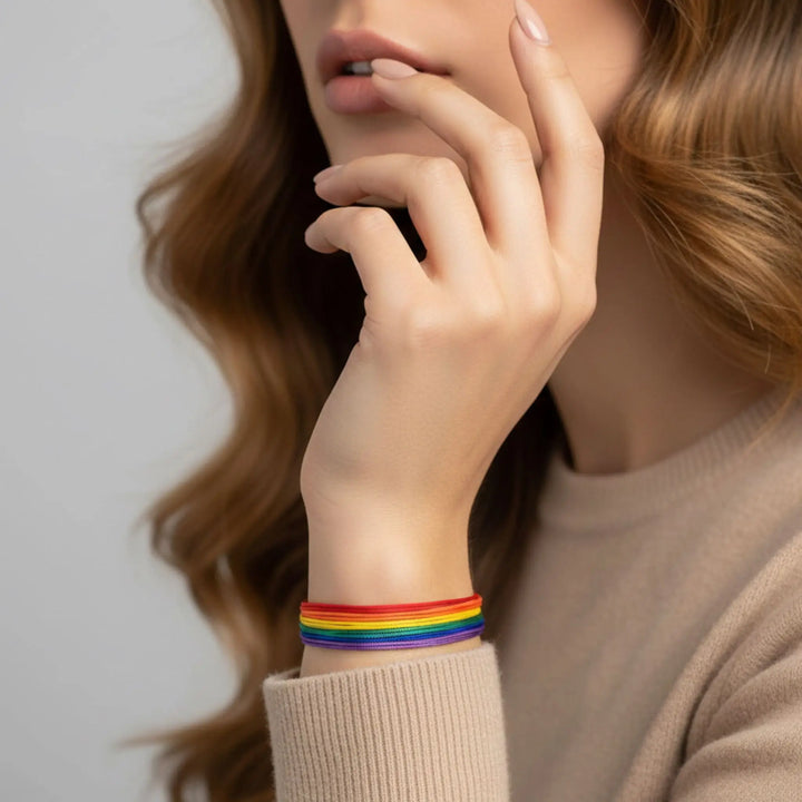 Person wearing a rainbow bracelet on a neutral background