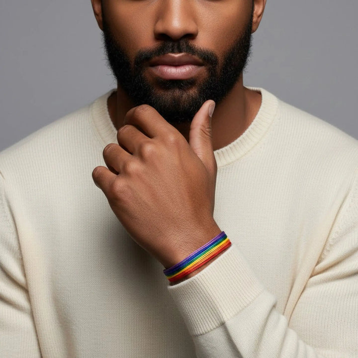 Man wearing a beige sweater with rainbow bracelets on a gray background