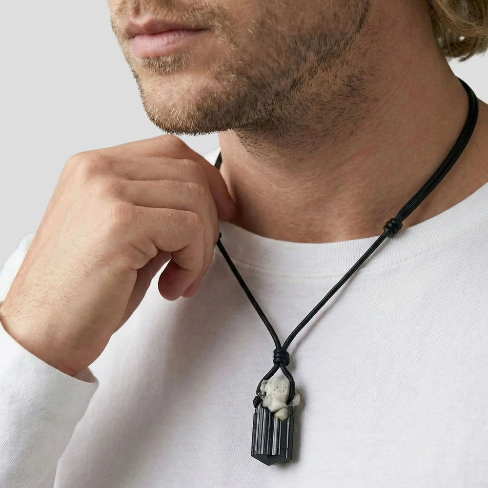 Man wearing a necklace with a raw black tourmaline pendant on a plain background