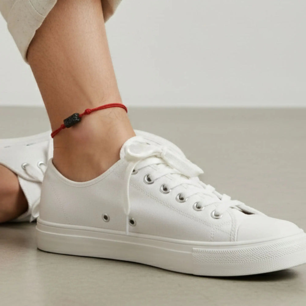 White sneakers worn with a black tourmaline red cord anklet on a neutral background