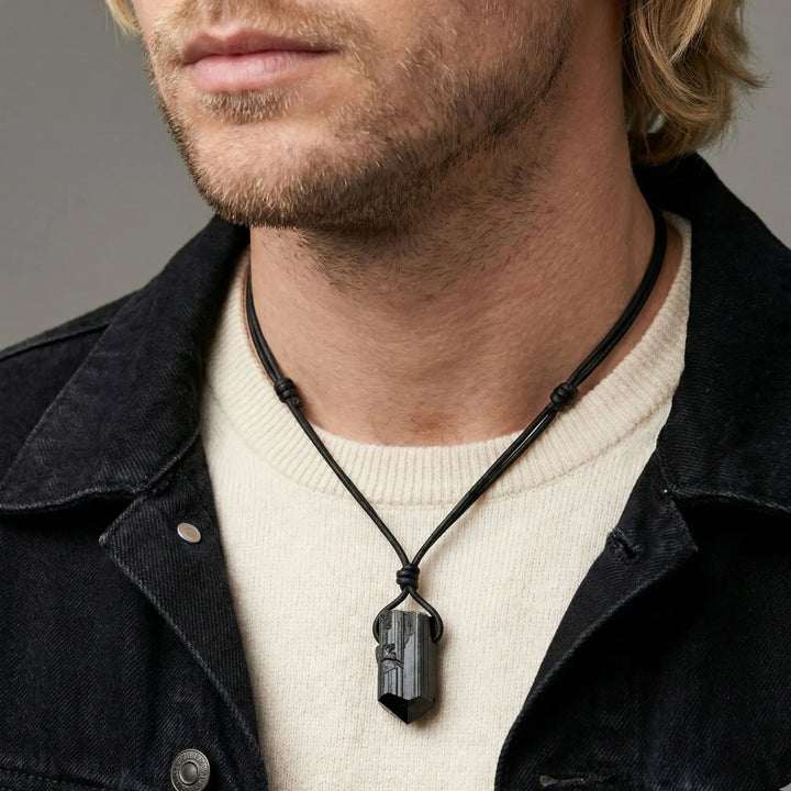 Man wearing a black tourmaline necklace with a pendant against a gray background