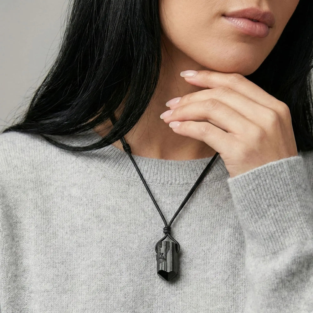 Person wearing a necklace with a black tourmaline pendant, touching their chin against a neutral background