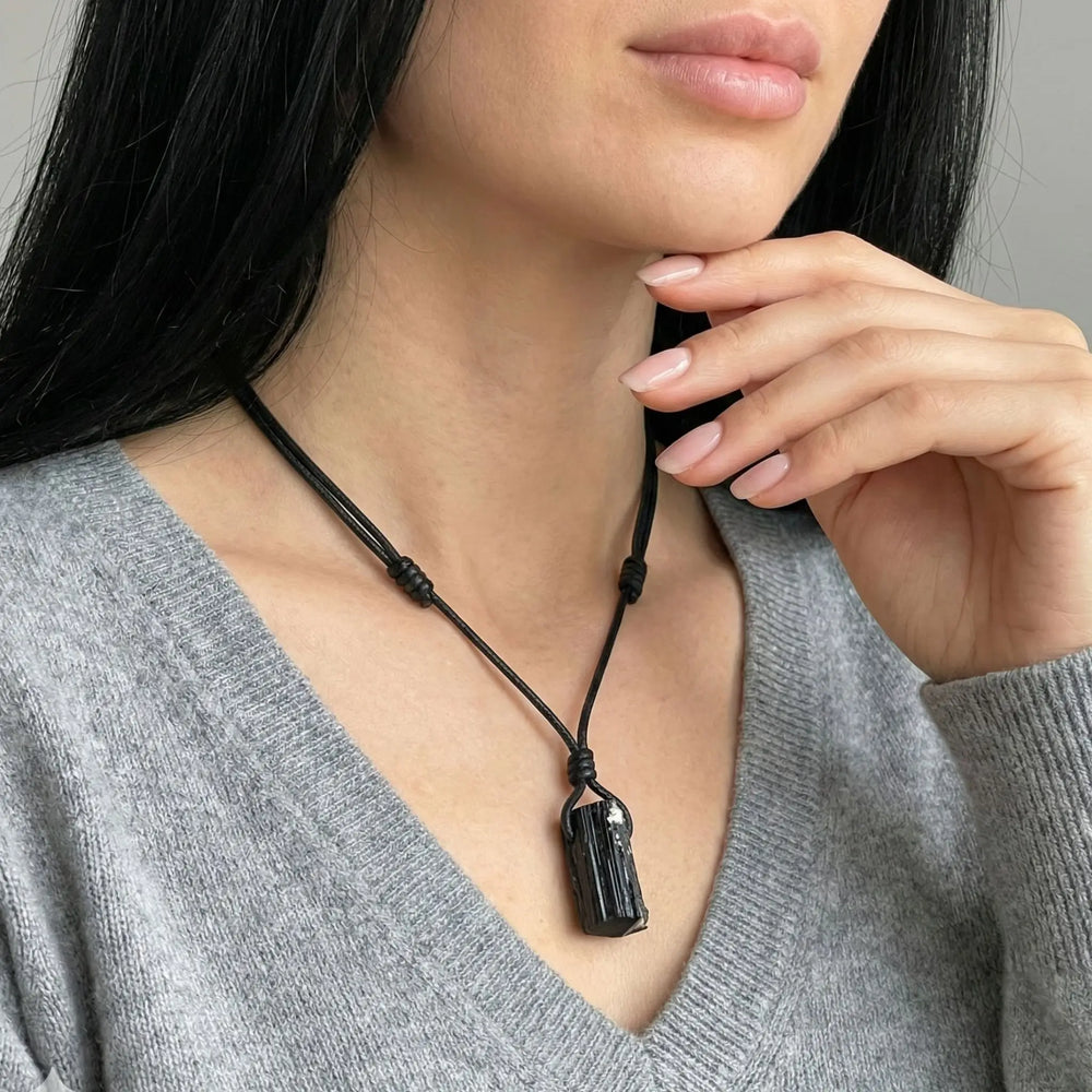 Person wearing a black necklace with a pendant, touching their chin.