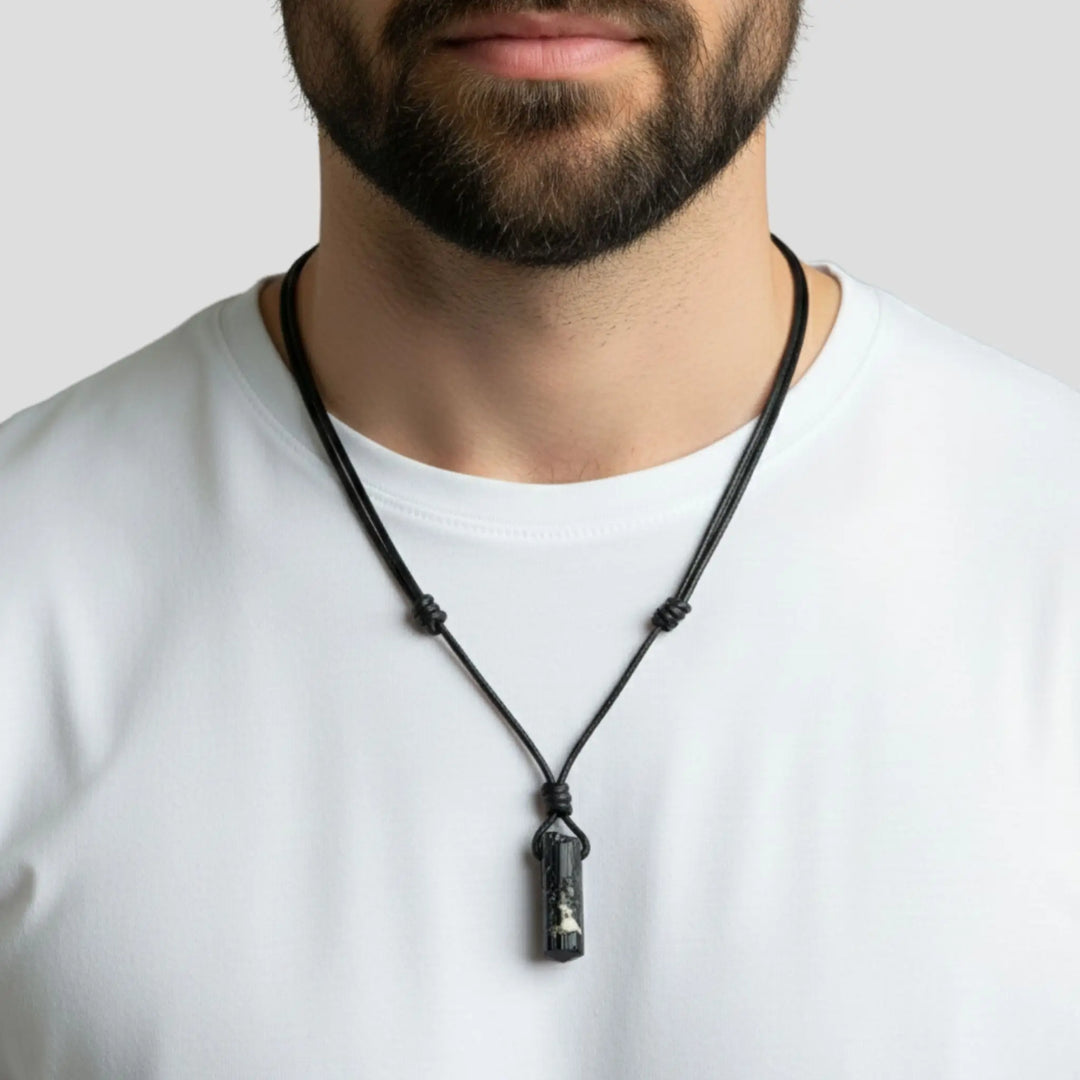 Man wearing a black tourmaline necklace with a pendant on a plain background