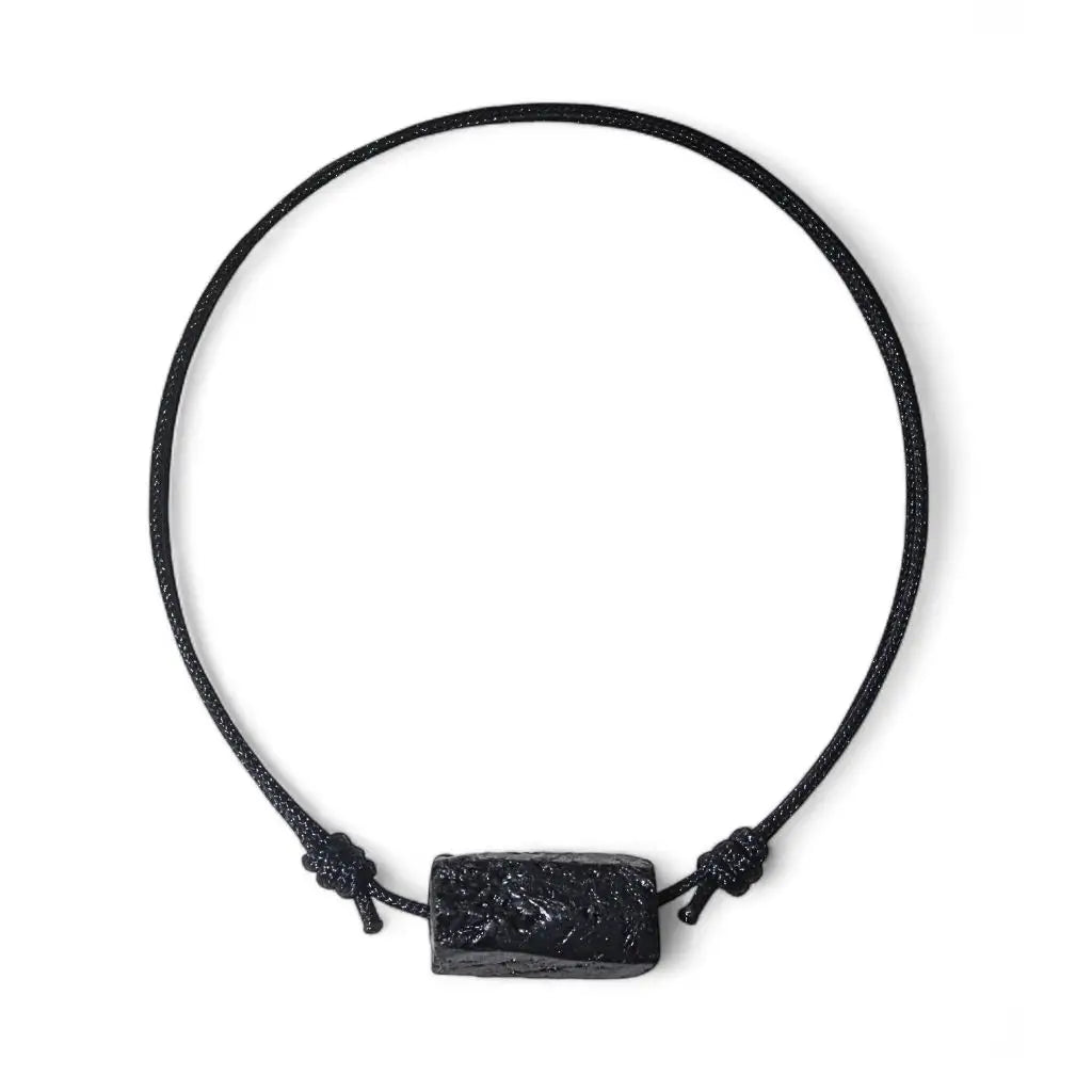 A black tourmaline energy bracelet with a raw crystal tube bead and nylon cord on a white background.