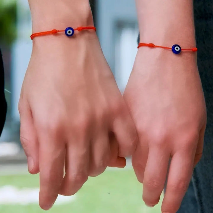 Hands together showcasing red string bracelets with evil eye charms, unisex style - Luck Strings.