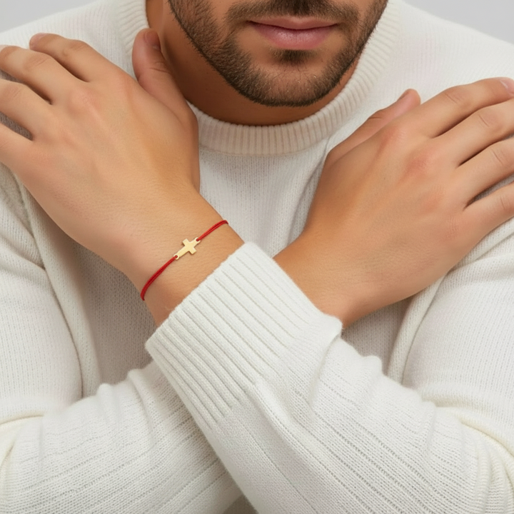 Person wearing a red bracelet with a gold cross on a white sweater.