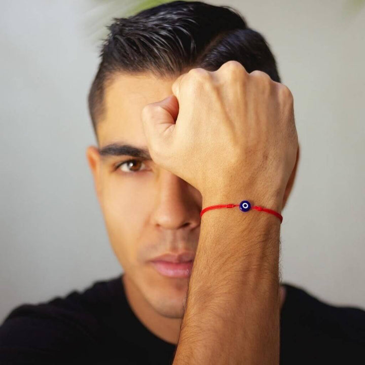 men wearing a red bracelet with a blue eye design on a neutral background