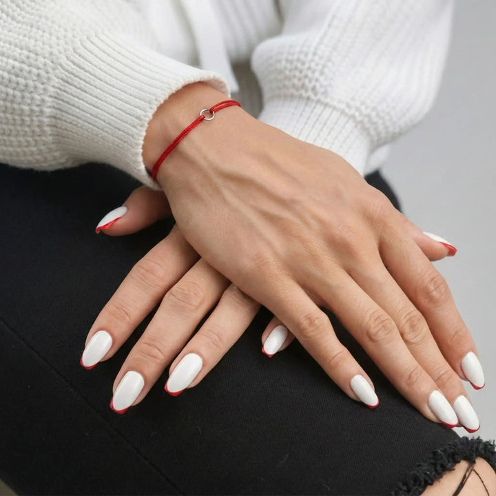 Close-up of hands with white nail polish and a red bracelet on a neutral background