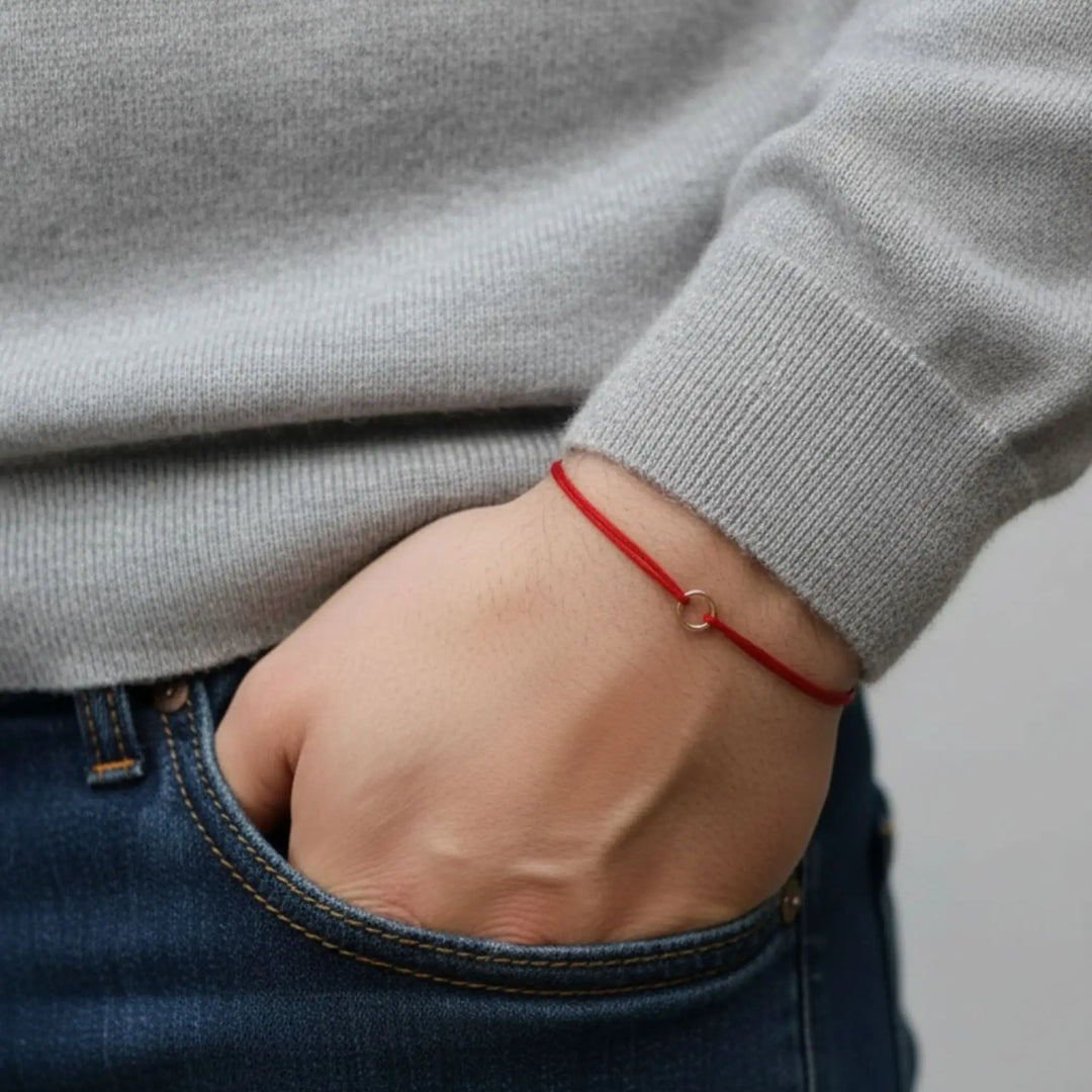 Person wearing a red bracelet on a neutral background