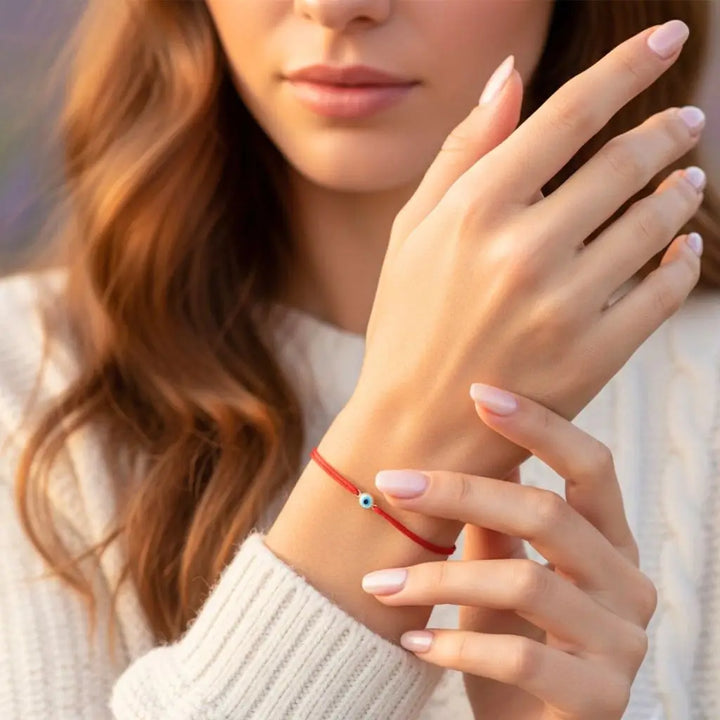 Close-up of a woman's hand wearing a red evil eye bracelet with a blurred background