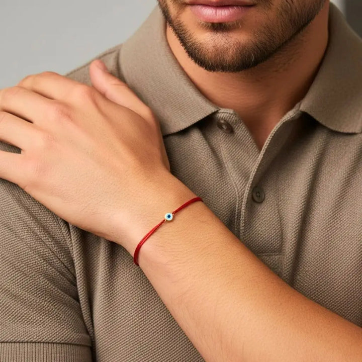 Close-up of a person wearing a red bracelet with a gold evil eye on a neutral background