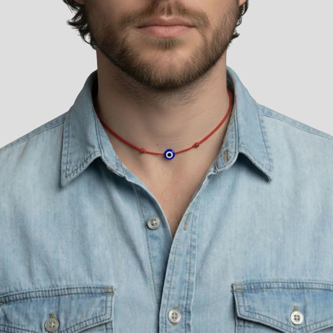 Man wearing a denim shirt with a red evil eye necklace featuring a blue and white eye pendant.