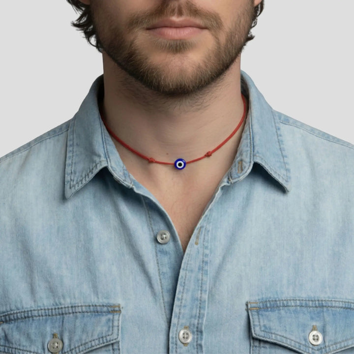 Man wearing a denim shirt with a red evil eye necklace featuring a blue and white eye pendant.