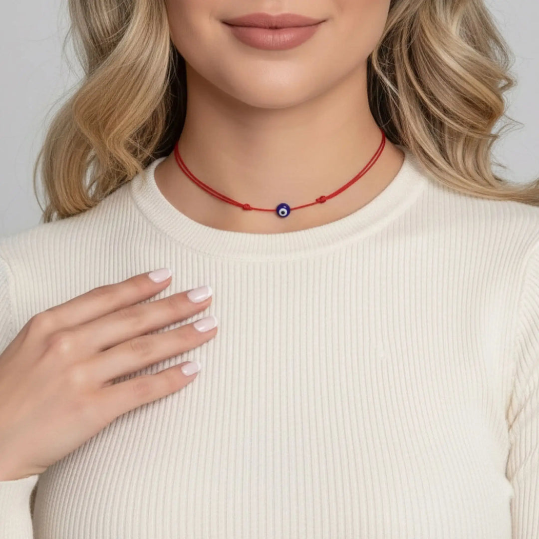 Woman wearing a red necklace with a blue evil eye pendant on a plain background