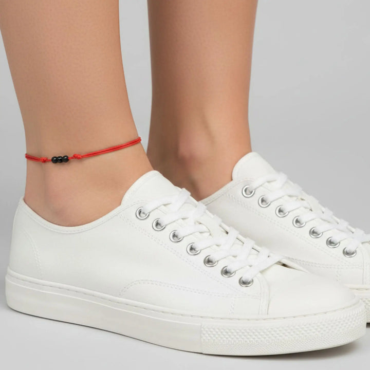 White sneakers worn with a black tourmaline red anklet on a neutral background