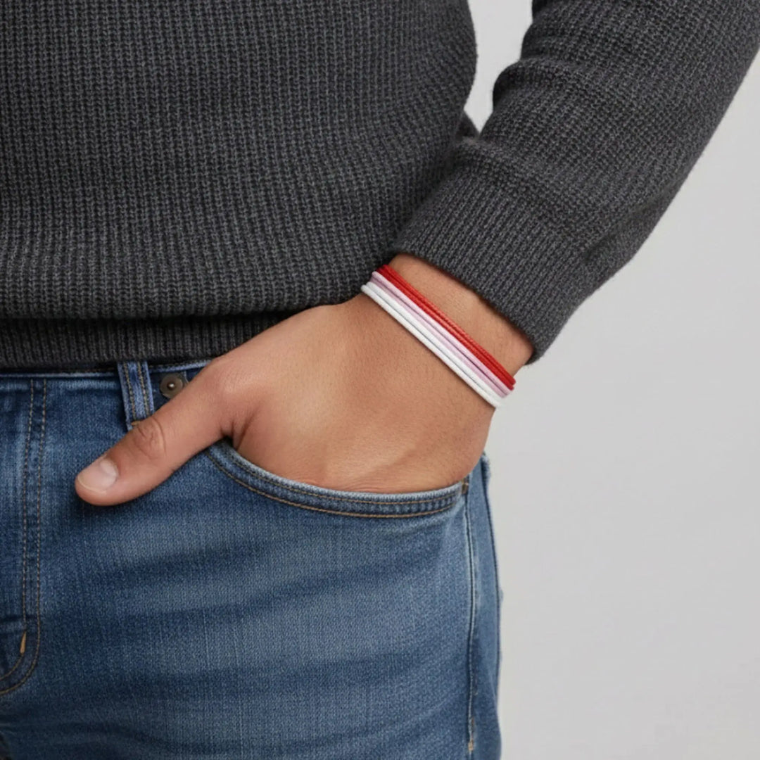 Person wearing a dark gray sweater and blue jeans with a red, pink, and white bracelet trio on a light gray background