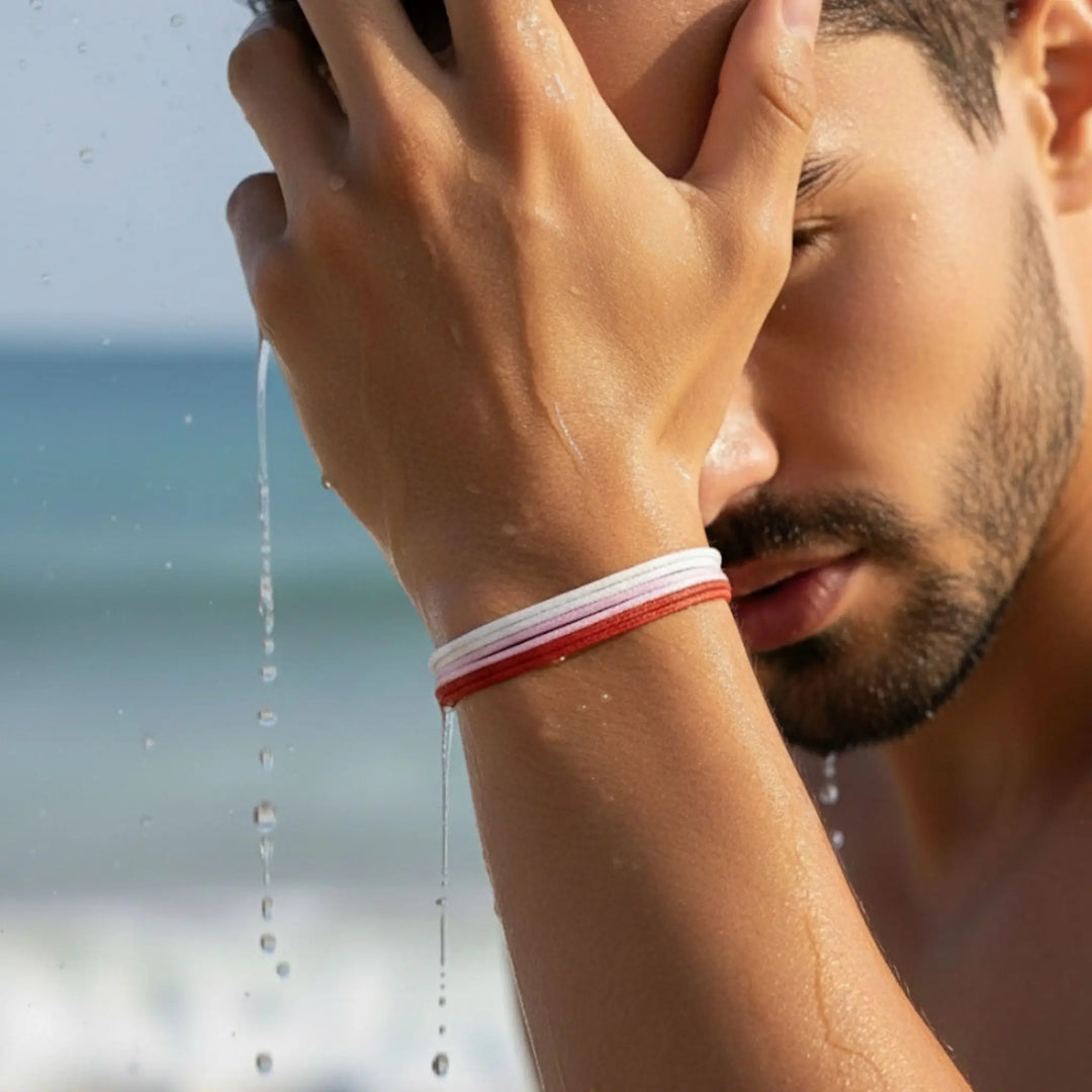 Man with a red, pink and white bracelet washing his face at the beach