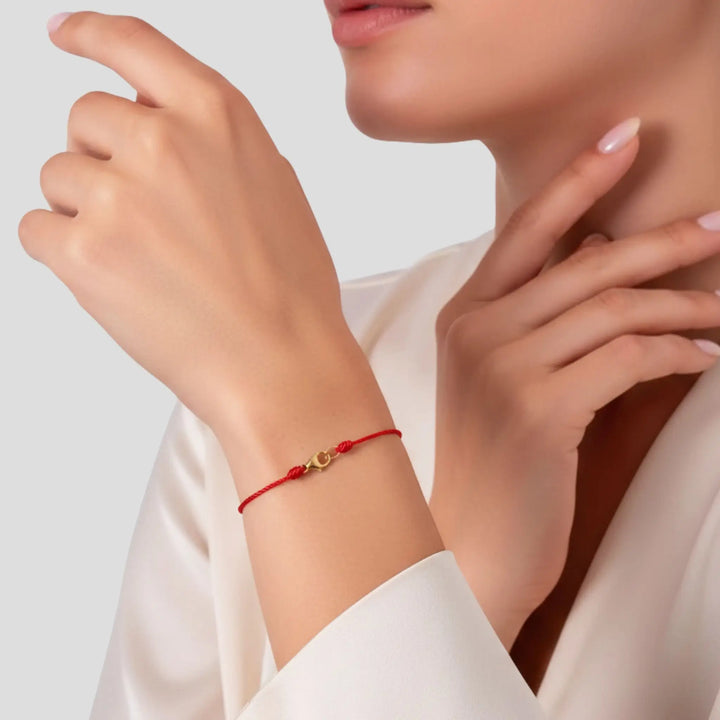Close-up of a person wearing a red bracelet with a gold charm on a neutral background