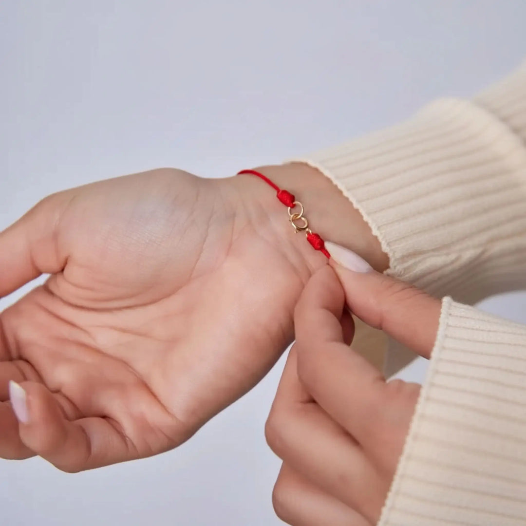 Two hands with a red string bracelet on a light gray background