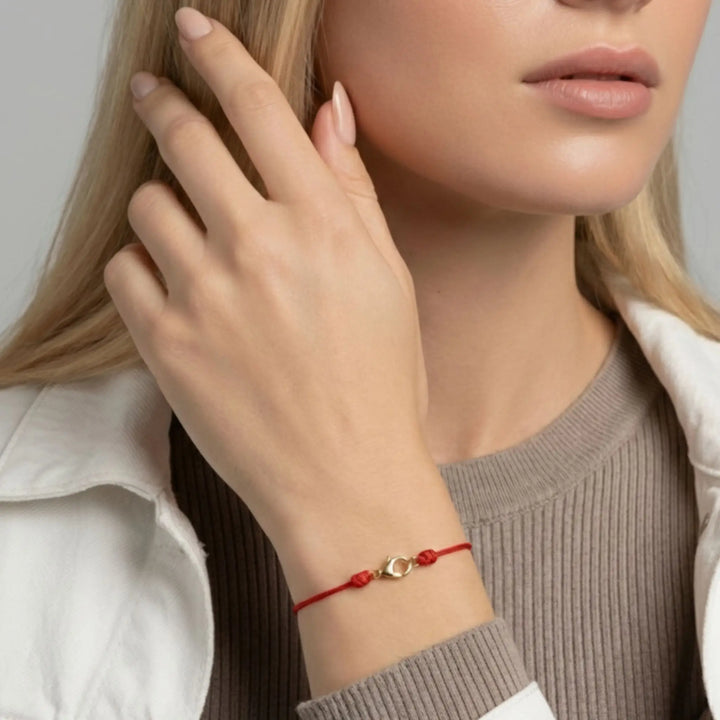 Close-up of a person wearing a red bracelet with a gold charm on a neutral background