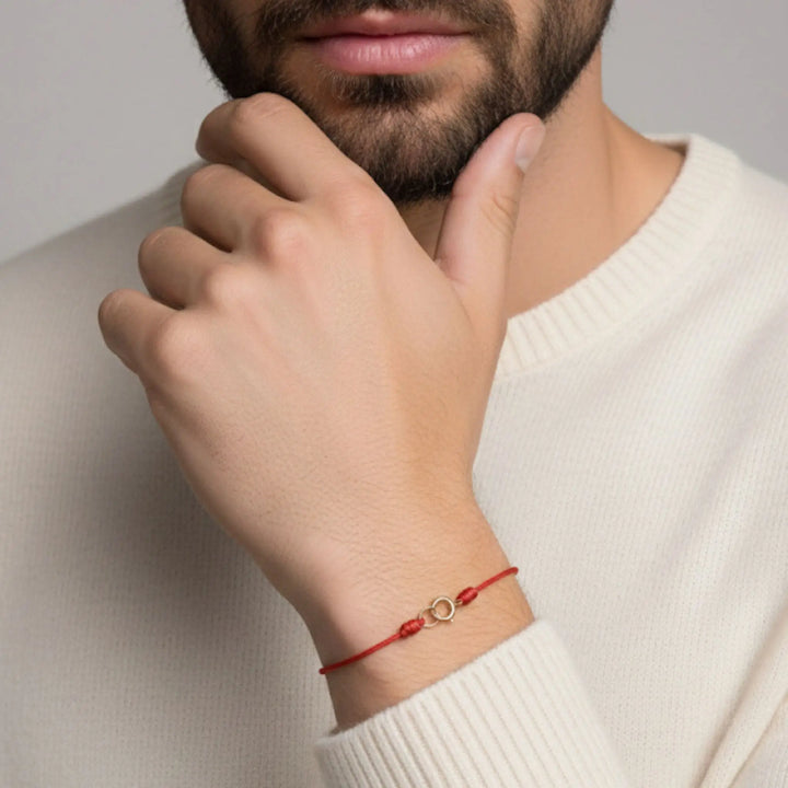Person wearing a red bracelet with a gold charm on a neutral background