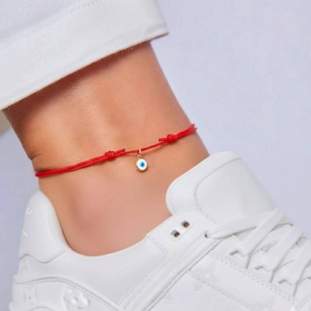 Red anklet with a small charm on a person's ankle against a white background