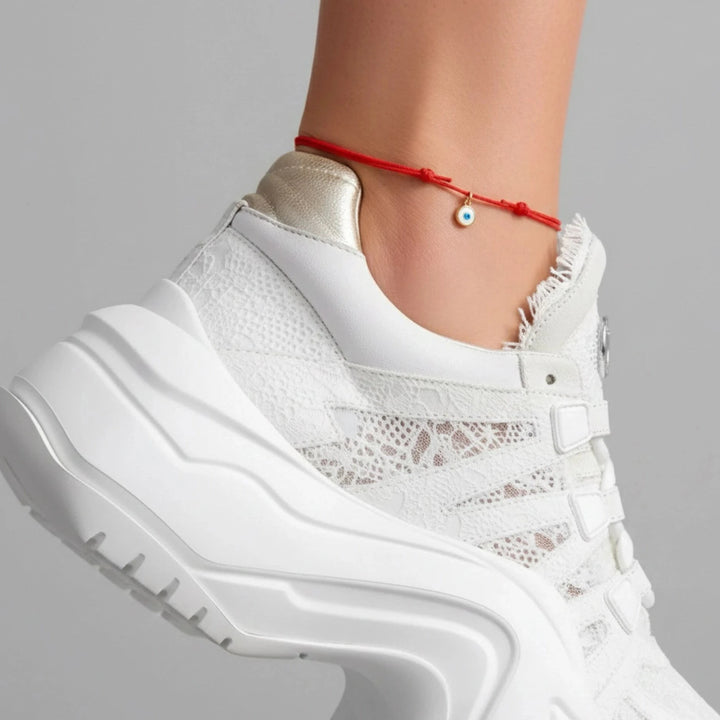 White sneaker with a evil eye red anklet with lace details worn by a person on a gray background 