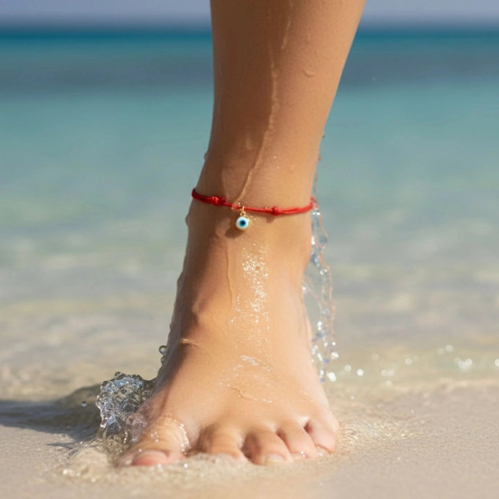 Foot with a red evil eye anklet on a beach