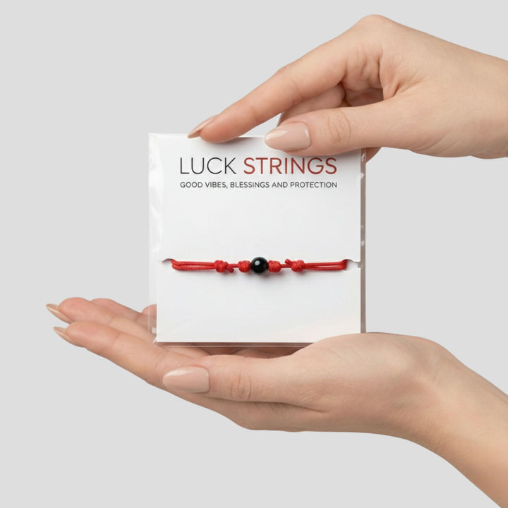Hand holding a red luck string bracelet with a black bead against a white background