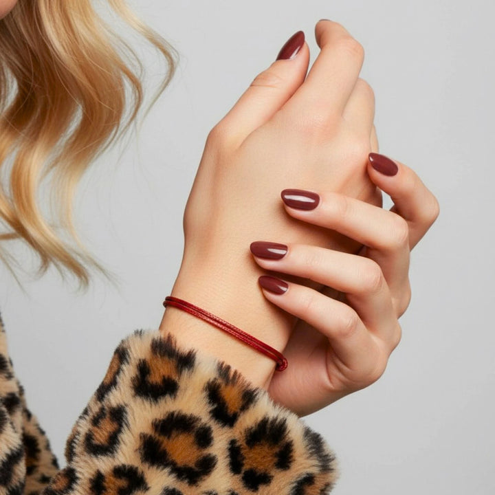 Close-up of a person's hands with red nail polish and a leopard print sleeve on a light gray background