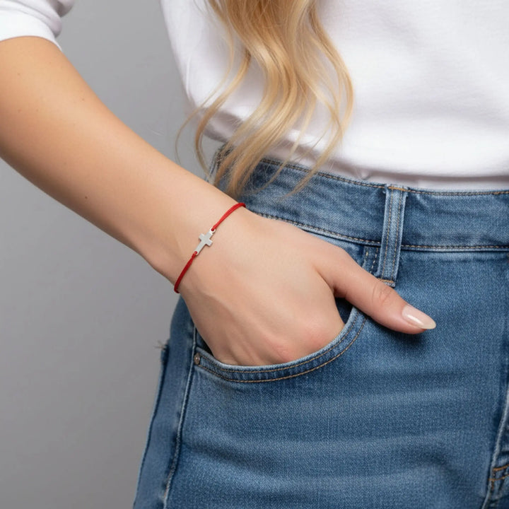 Person wearing a red bracelet with a silver cross on a plain background