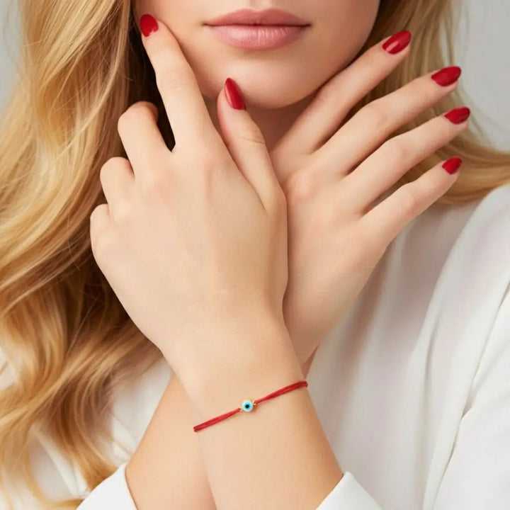 Close-up of a woman's hands with red nail polish and a red gold evil eye bracelet on a white background