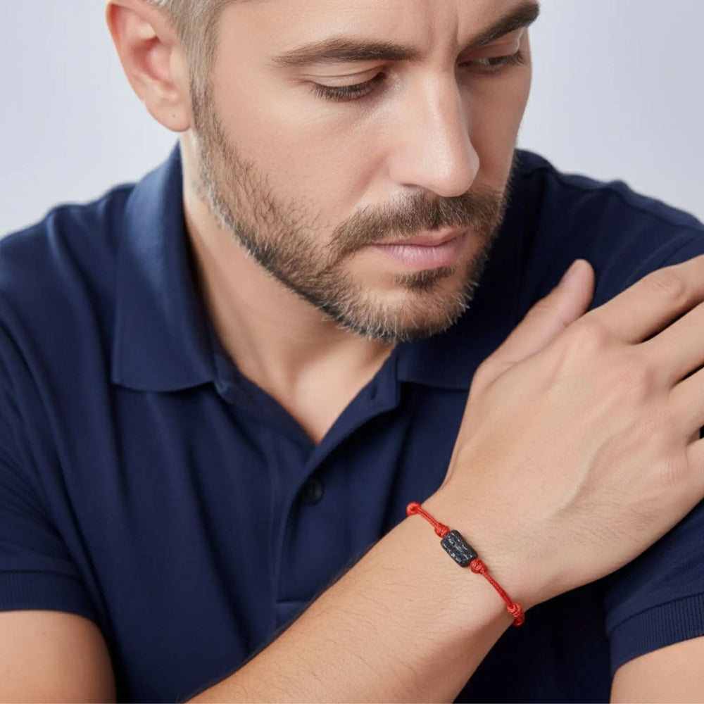 Man wearing a red bracelet with a black tourmaline, looking down.
