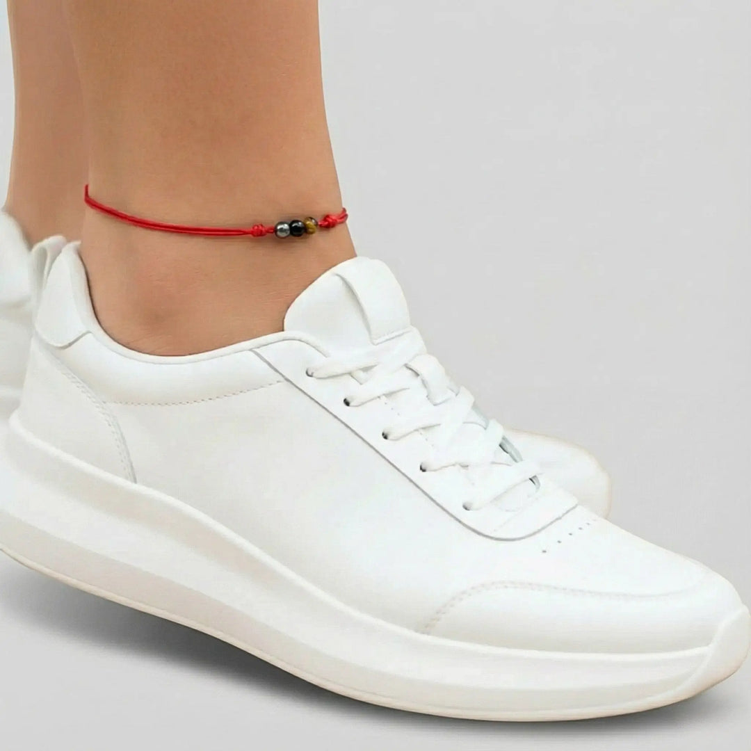 White sneakers worn with a red anklet on a neutral background