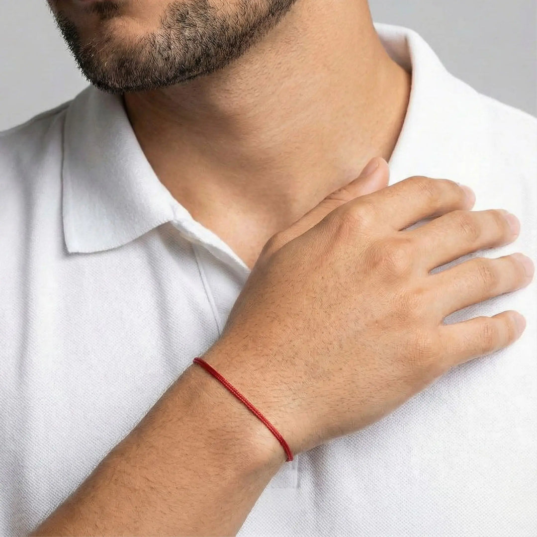 Man wearing a red string bracelet on his wrist, with a neutral background
