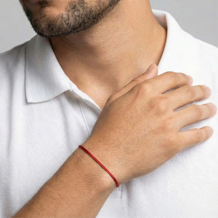 Man wearing a red string bracelet on his wrist, with a neutral background