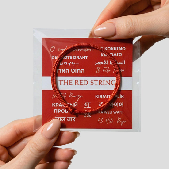 Red string bracelet held by a hand with a red packaging label in the background