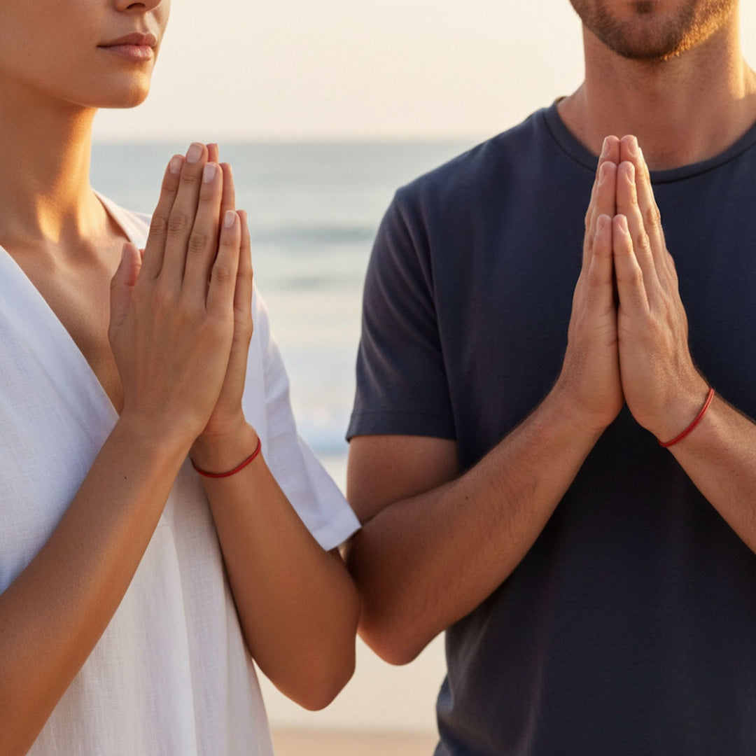 Two people with hands pressed together in a prayer position on a beach.