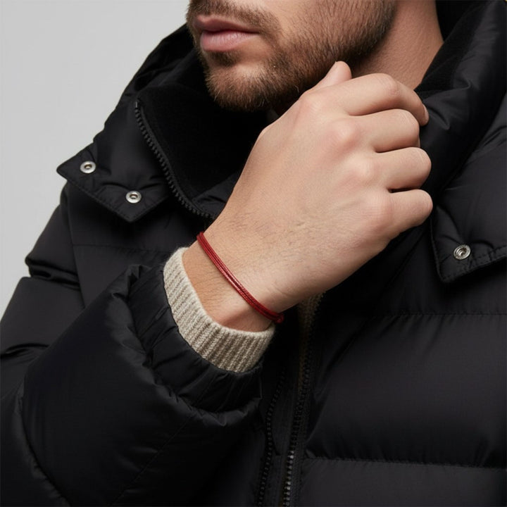 Person wearing a black jacket with a red bracelet on a gray background