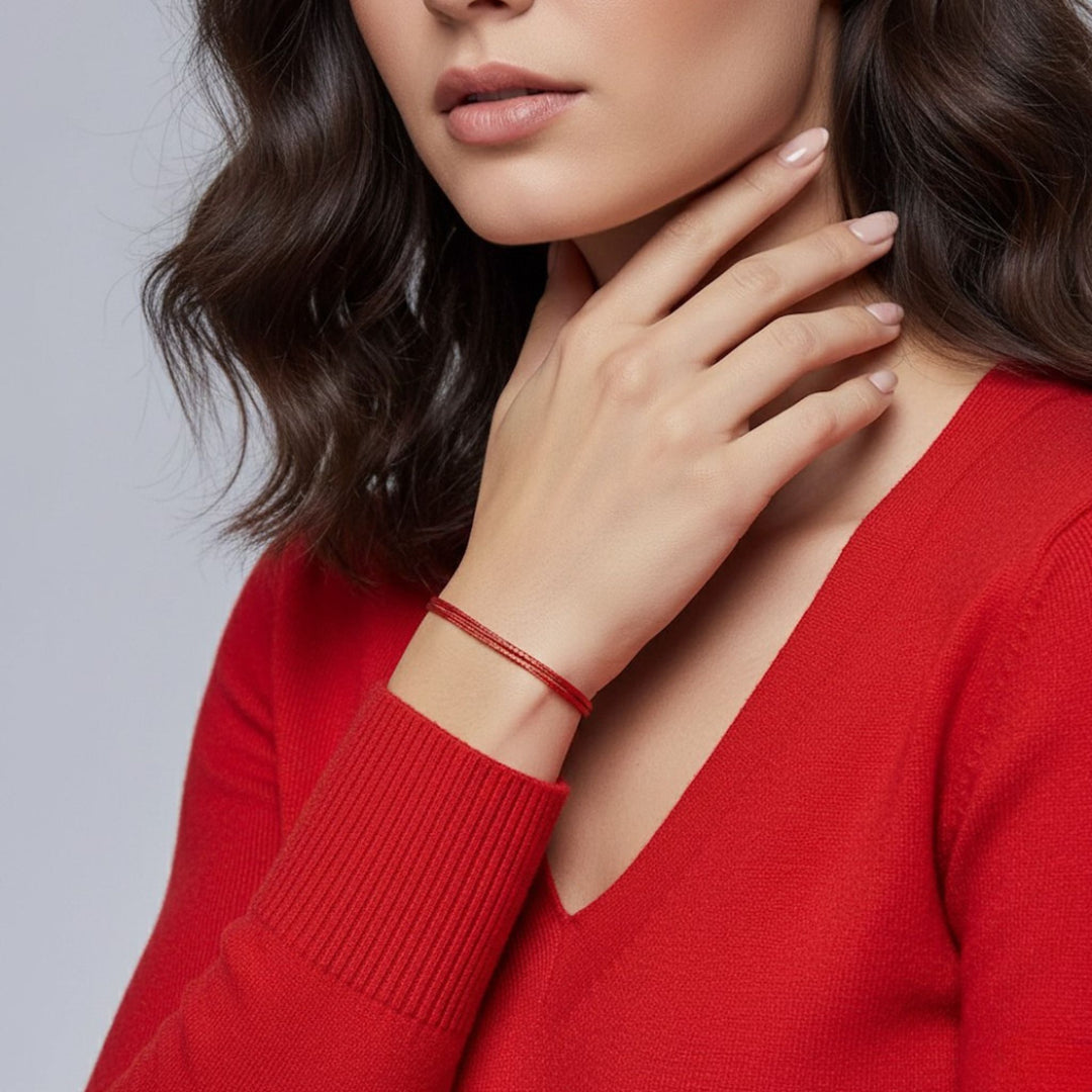 Woman wearing a red sweater with a close-up of her hand and bracelet on a gray background