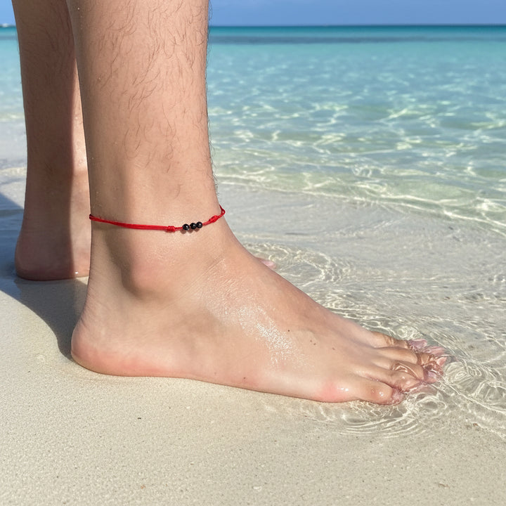 Adjustable tourmaline red string anklet with 4mm beads, modeled on a woman's ankle, symbolizing protection and good luck 