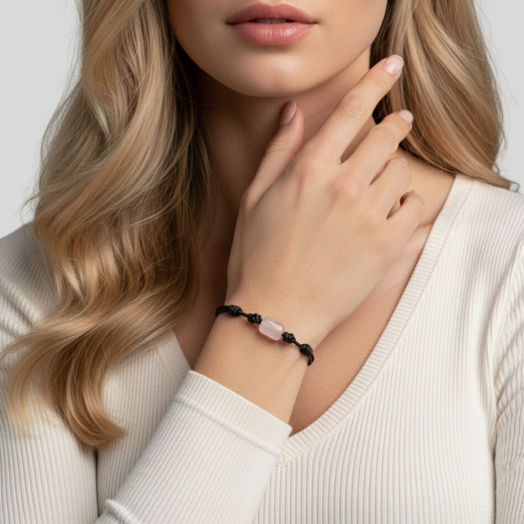 Woman wearing a bracelet with a rose quartz stone on a plain background