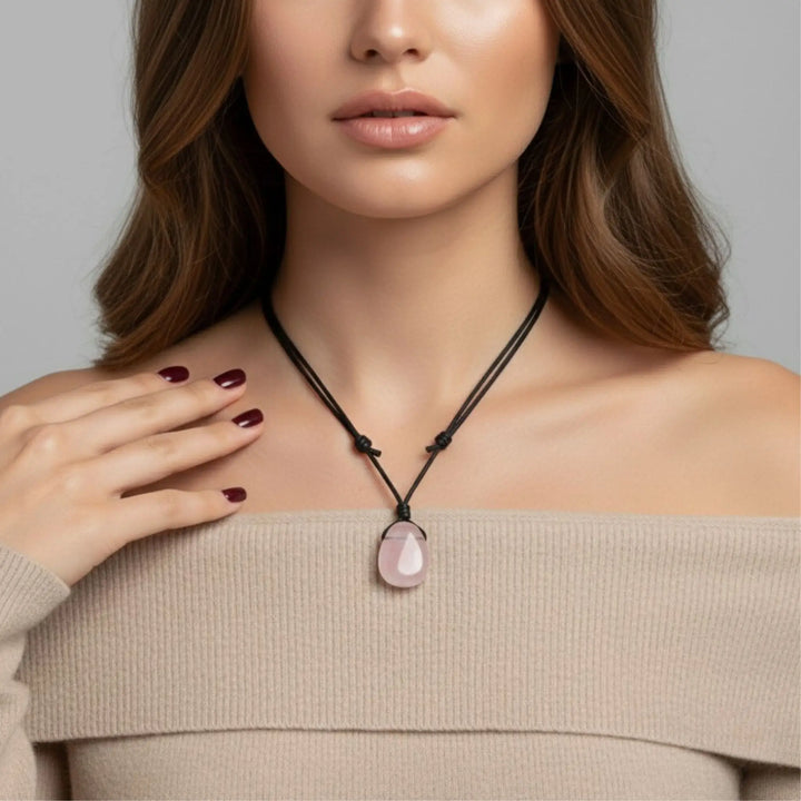 Woman wearing a necklace with a rose quartz pendant against a neutral background
